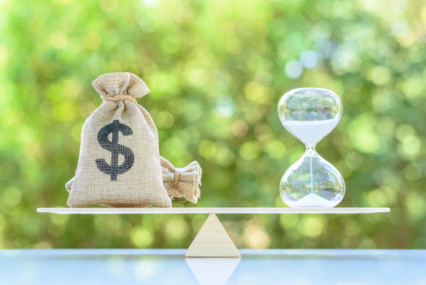 An hourglass and a stack of money balanced on a scale, symbolizing the relationship between time and wealth.
