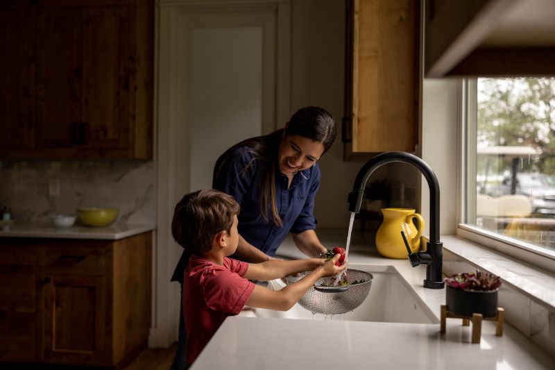 A mother washing fruit in the sink with her son.