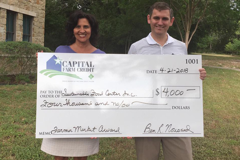 A man and woman smiling and holding up a large check