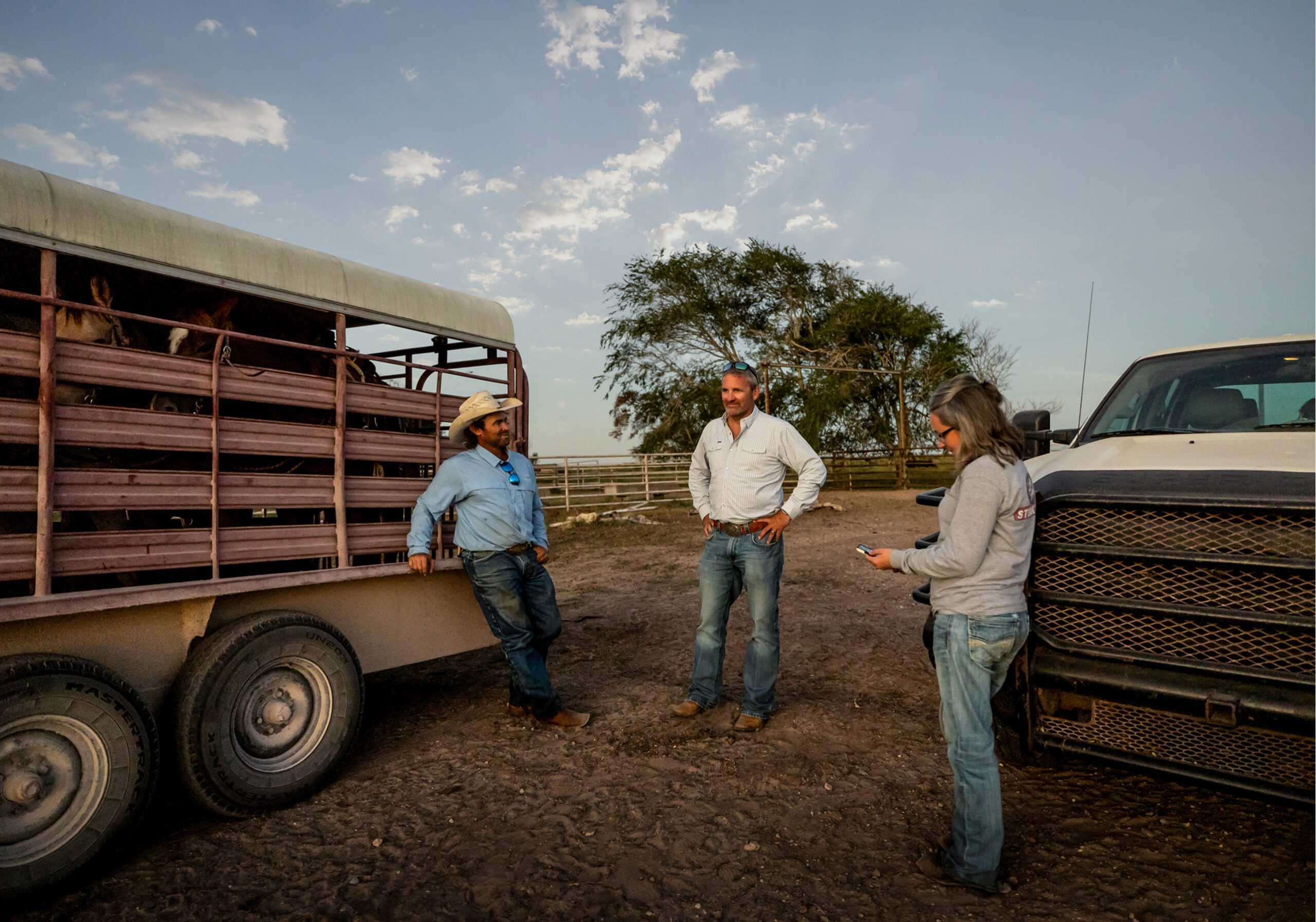 Three people chatting next to a pickup truck and horse trailer