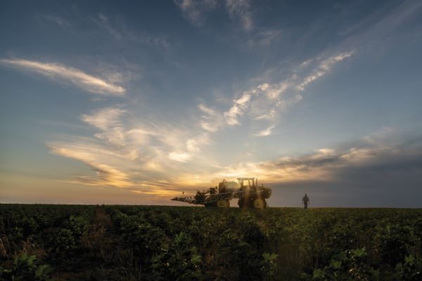 A tractor and a man are positioned in a field during sunset, surrounded by golden light and a colorful sky.