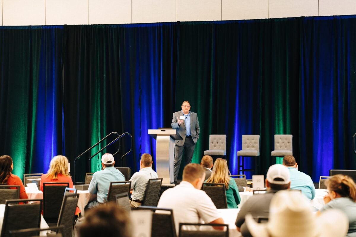 A man stands behind a podium addressing conference goers