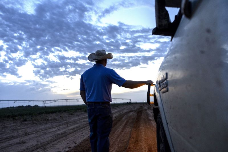 A man in a cowboy hat poses next to a truck, surrounded by open land.