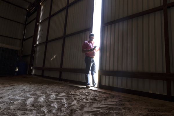 A man stands in a sunlit barn, with sunlight streaming through the open door, illuminating the rustic interior.