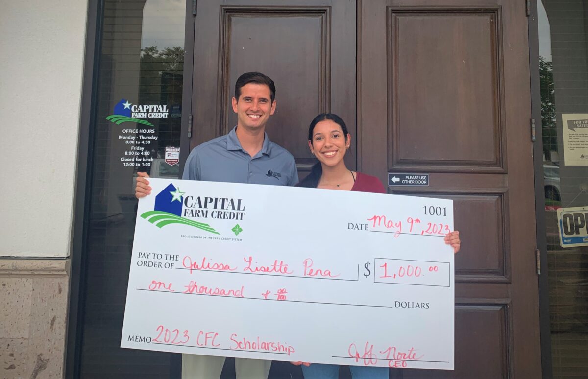 A Capital Farm Credit employee holding a large scholarship check with the recipient.