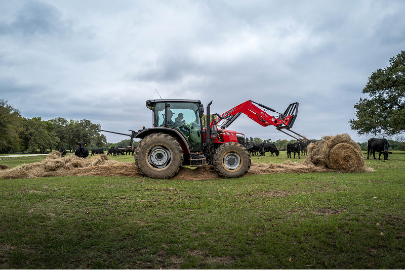Two farmers in a utility loader unrolling a hay bale