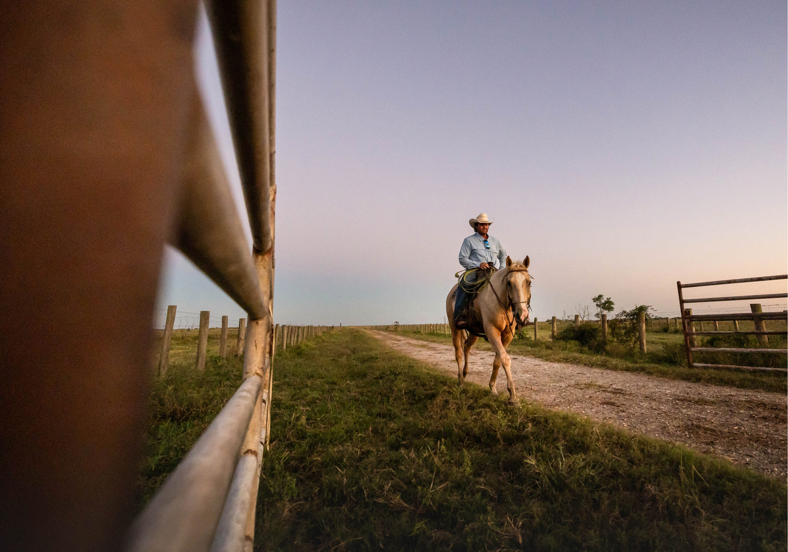 a rancher riding his horse down a dirt road at dusk