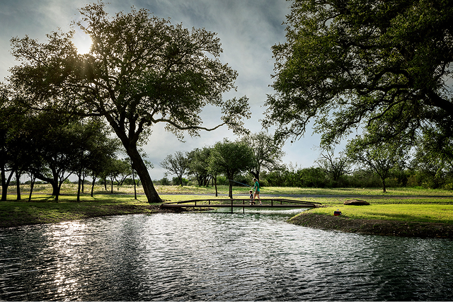 a distant view of a woman and child crossing a small footbridge over a pond