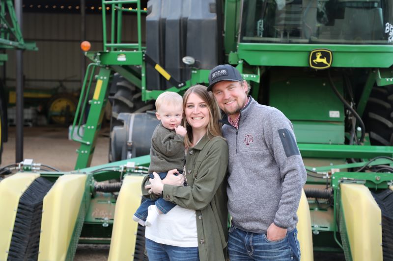 Anthony and Jayci Bishop with their son posing in front of harvesting equipment
